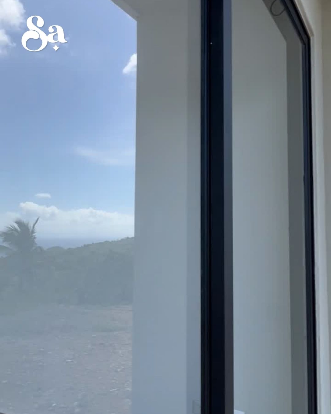 Wideo przedstawiające wnętrze willi Flat House widoczne przez jej duże panoramiczne okna, z widokiem na ocean i otaczającą tropikalną zieleń.