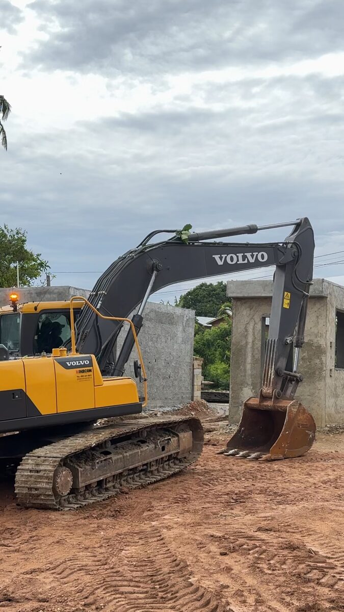 An excavator beside a freshly cast reinforced concrete column on a cleared building platform