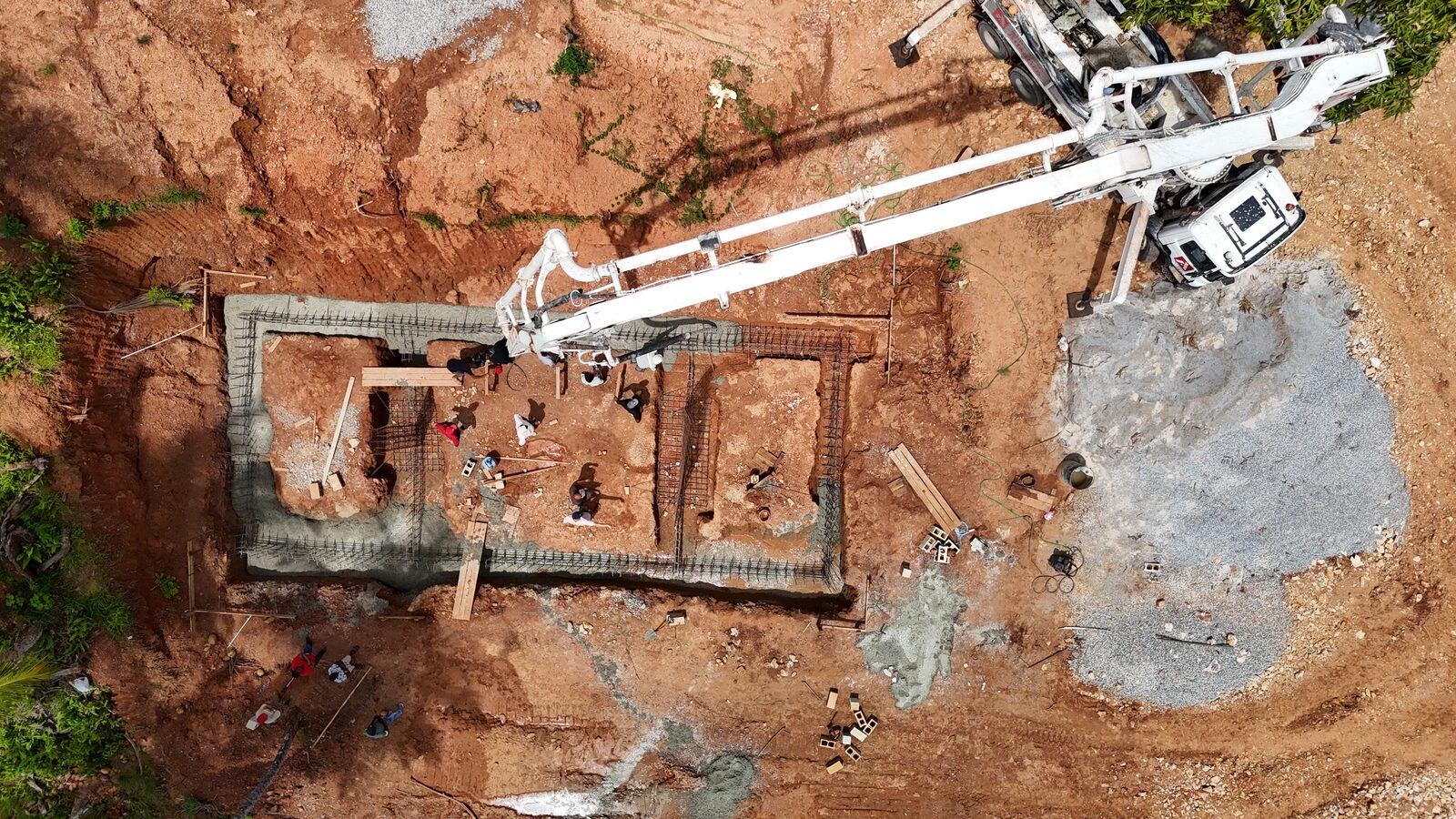 Aerial view of a rectangular reinforced concrete foundation with formwork and an excavator alongside