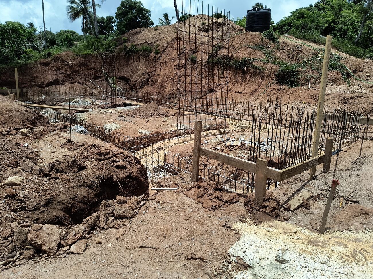 Reinforcement cages standing in an excavated foundation trench cut into red earth