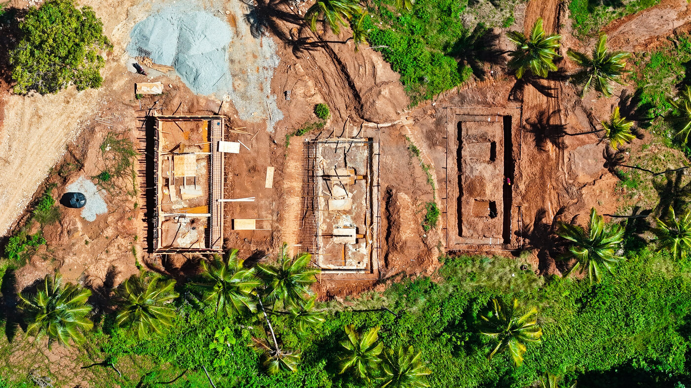 Aerial view looking down on three houses under construction with walls up, surrounded by palms