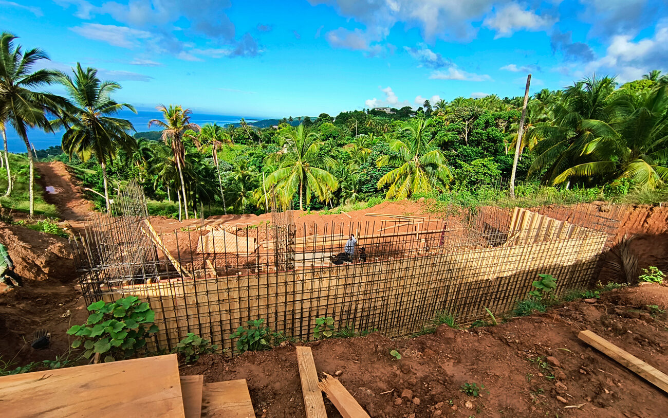 A reinforced retaining wall under construction with rebar and formwork, palms and the sea beyond