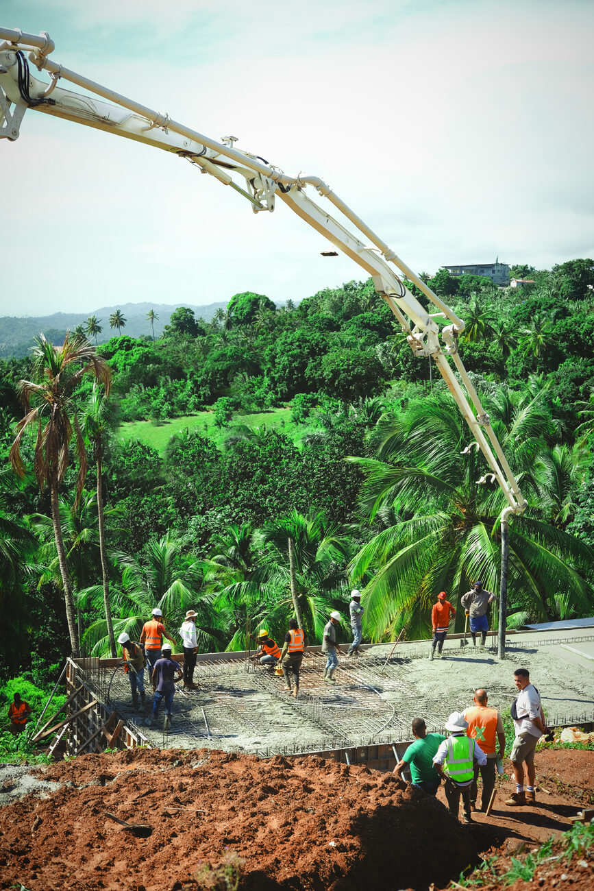 A concrete pump boom extended over a hillside plot with a crew placing and levelling concrete
