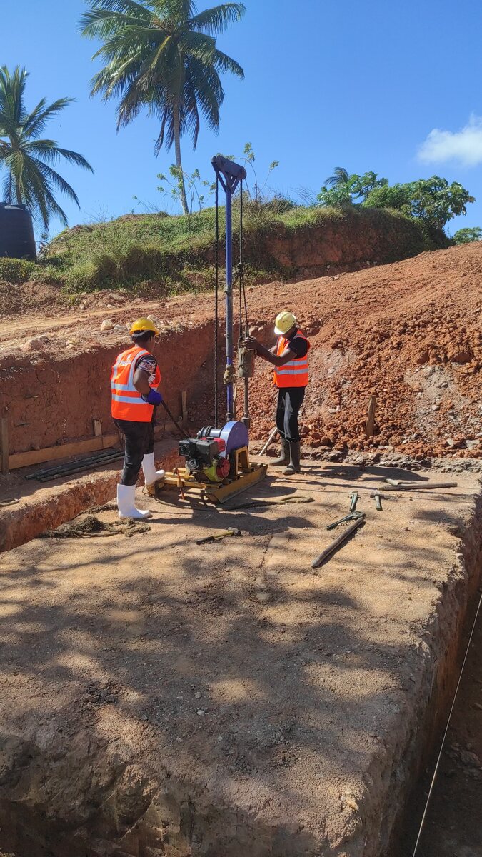 Two engineers in high-visibility vests operating a soil drilling rig on an excavated platform