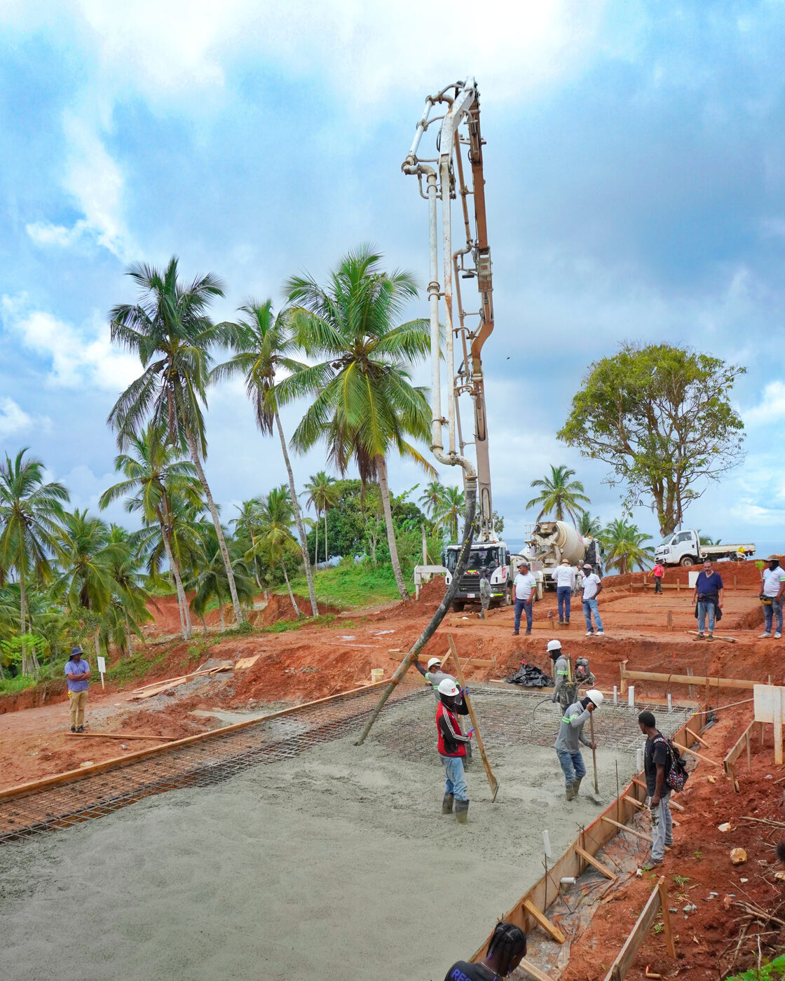 Concrete pump boom over a large poured slab with a crew of workers finishing the surface, palms behind