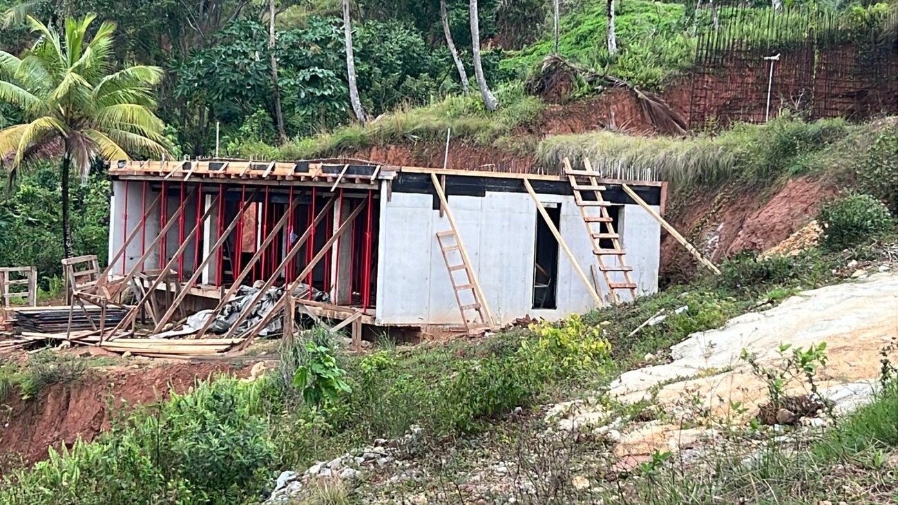 A house under construction on a hillside terrace, cast concrete walls up with red steel props and timber formwork supporting the roof slab
