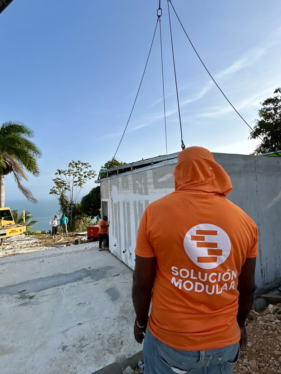 A worker in a Solución Modular hoodie watching a house module being lifted by crane on site