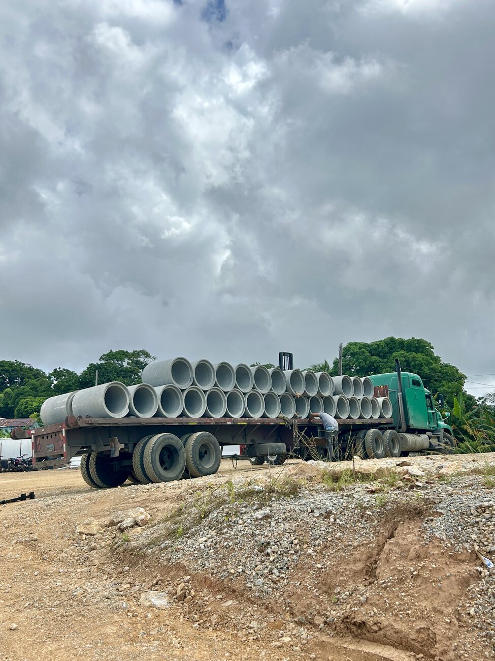 A flatbed truck loaded with two stacked rows of large concrete drainage pipes on a gravel yard