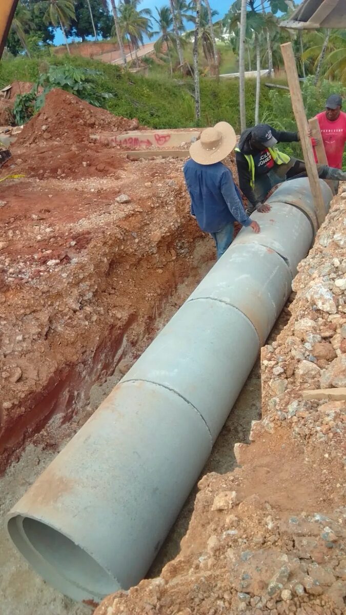 Workers positioning a large concrete drainage pipe in an excavated trench