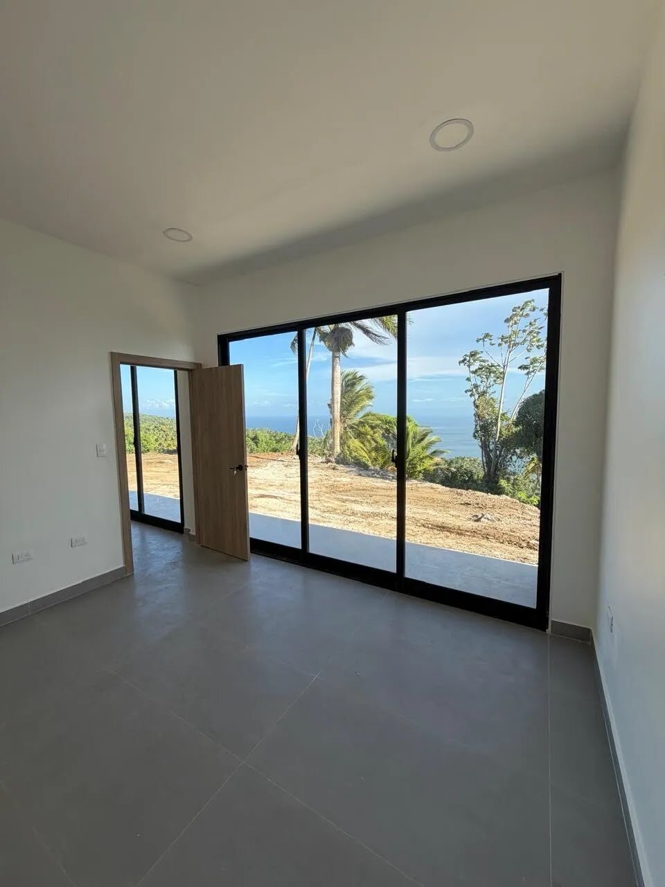 A second bedroom with tiled floor, a door to the terrace and glazing onto palms and the sea
