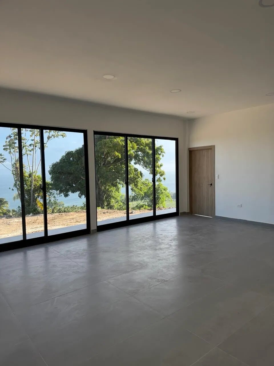 Interior living space with tiled floor and two sets of full-height sliding doors opening to trees and sea
