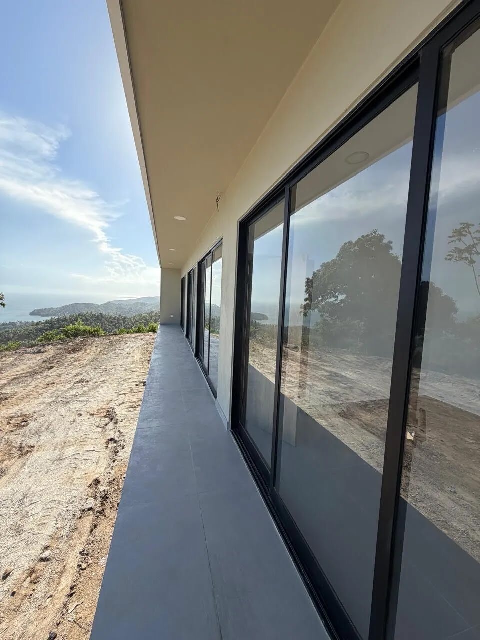 The covered terrace of the house running along the glazing, the bay and headlands beyond