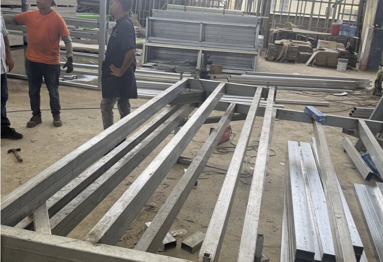 A long-span steel frame under fabrication on the plant floor with tube stock laid out alongside