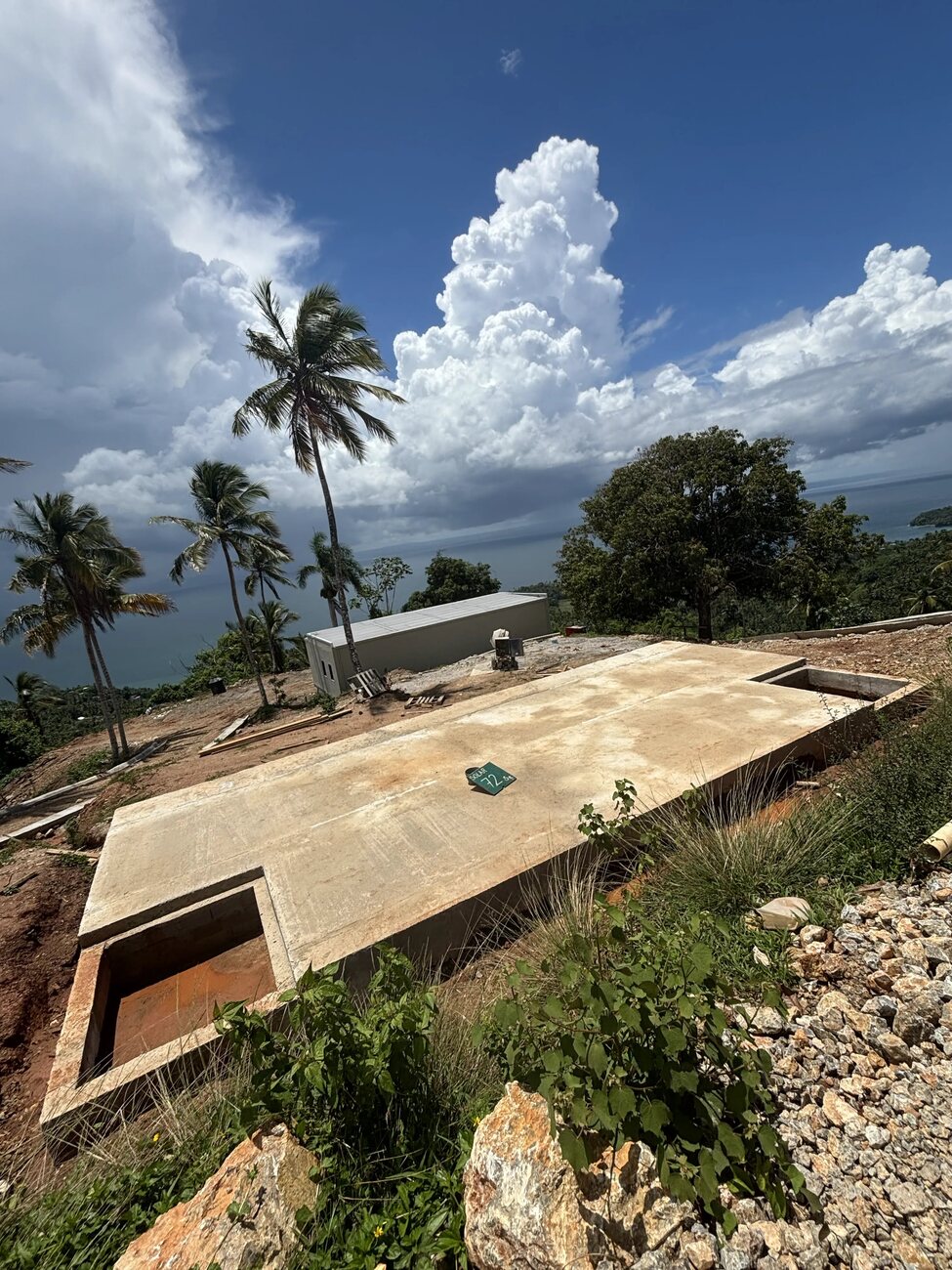 Close view of a poured concrete slab with a service pit formed at one end, palms and sea behind