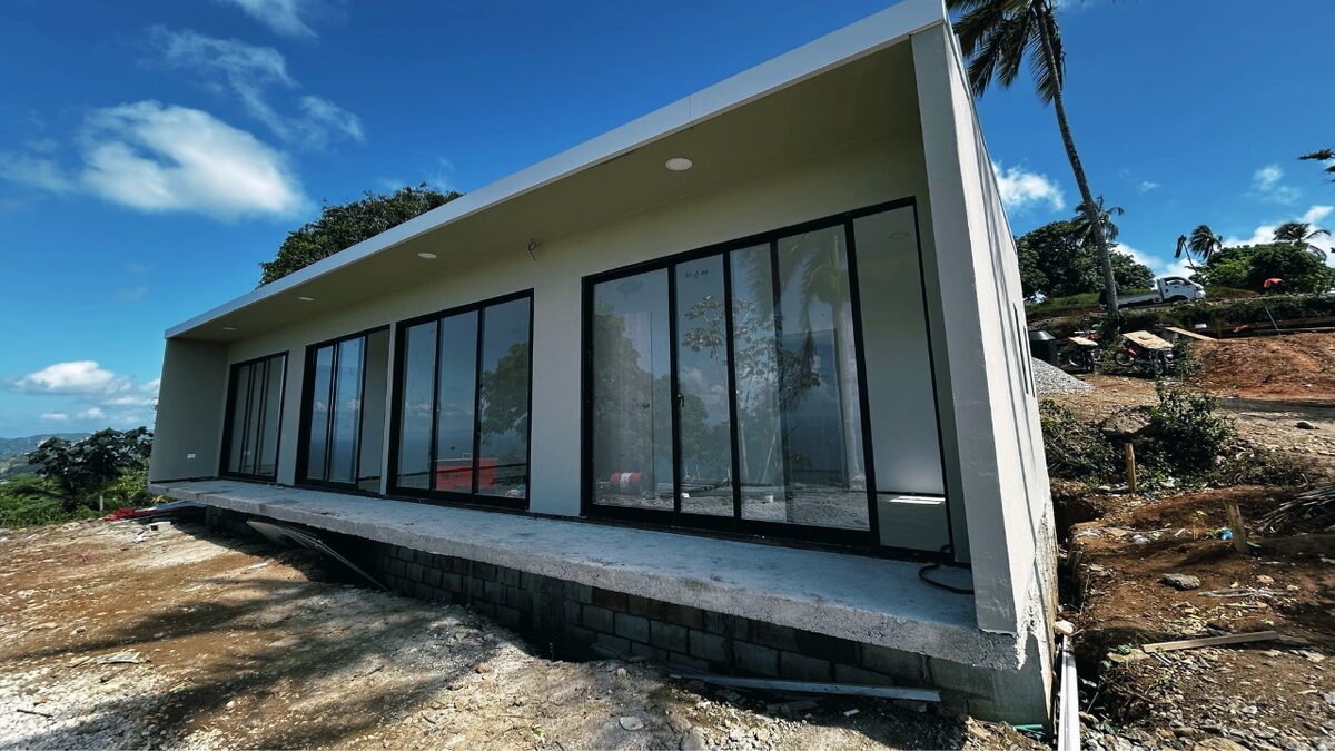 A completed single-storey Flat House villa with full-height glazing standing on a levelled site